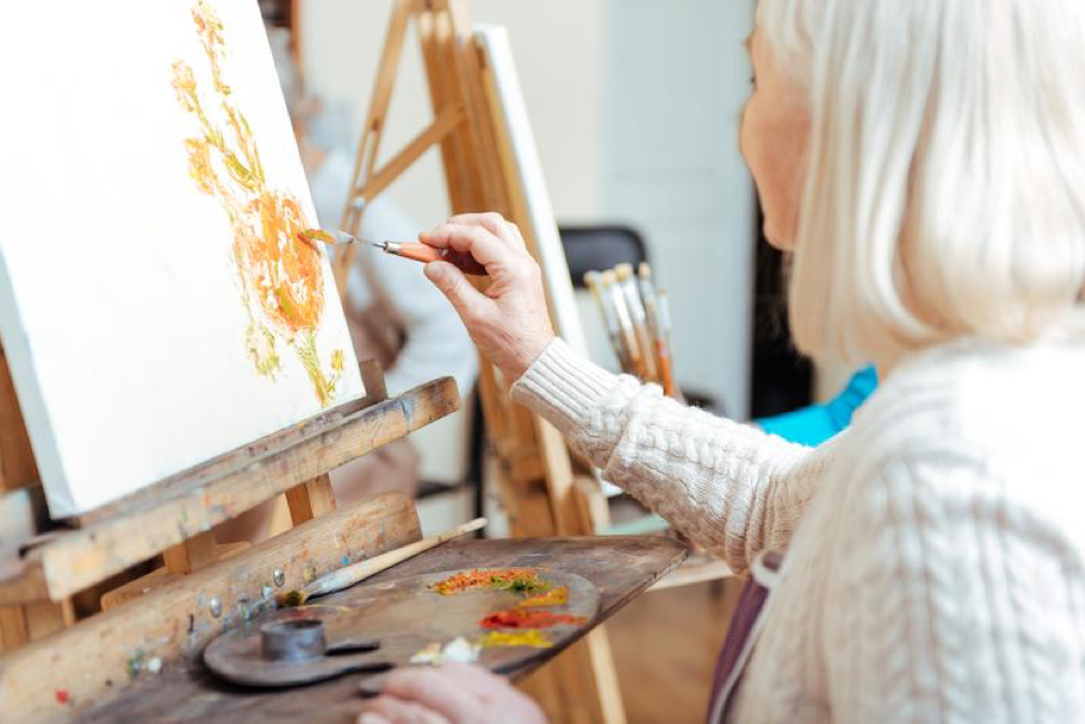 Elderly woman sits at an easel and paints